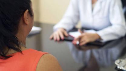 Rassismus im Gesundheitswesen: Rückenansicht einer BiPoC-Patient*in im Gespräch mit einer Person im weißen Kittel